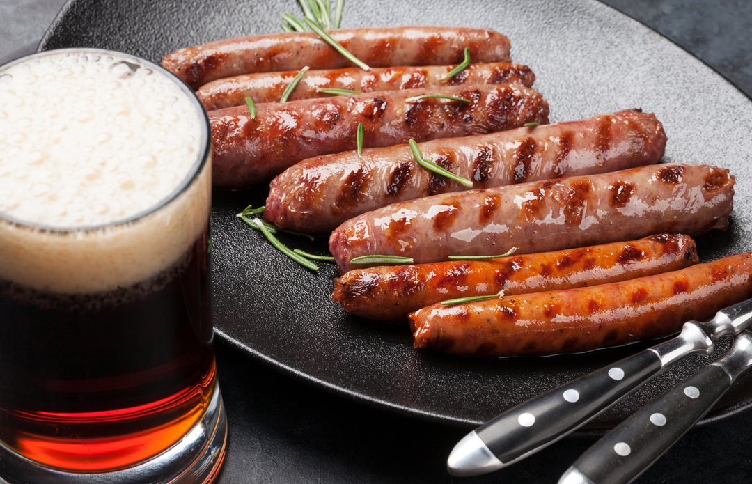 クラフトビールの黒ビールと焼いたソーセージをテーブルに並べた画像